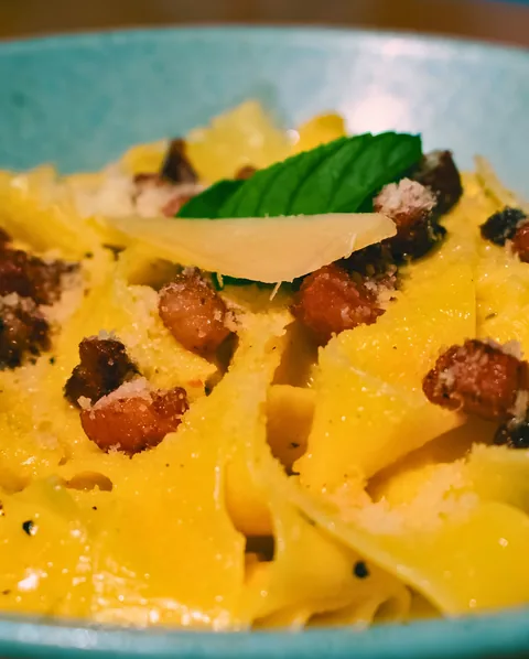 Acercamiento a unos pappardelle a la carbonara con guanciale dorado y una lámina de queso