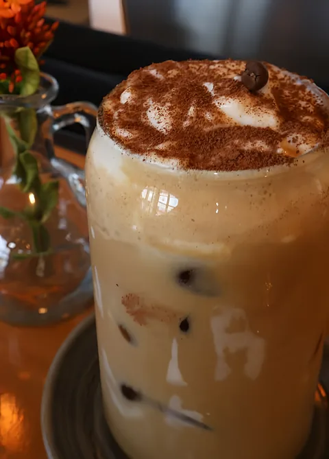 Latte frío en vaso de vidrio con cacao espolvoreado y un grano de café encima