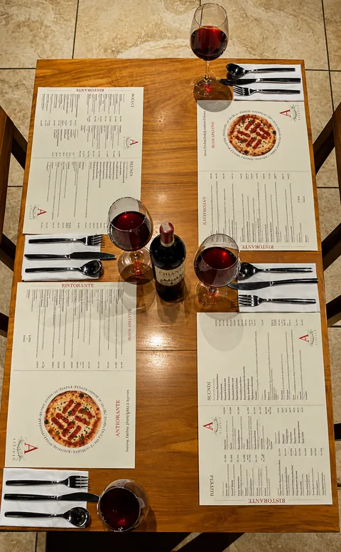 Vista desde arriba de una mesa para cuatro: cartas de Attilio, copas de vino tinto, una botella y cubiertos