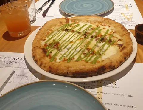 Pizza blanca con un hilo de salsa verde, sobre la carta y junto a un plato turquesa