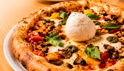 Pizza de vegetales con queso burrata al centro, hojas de albahaca y pesto
