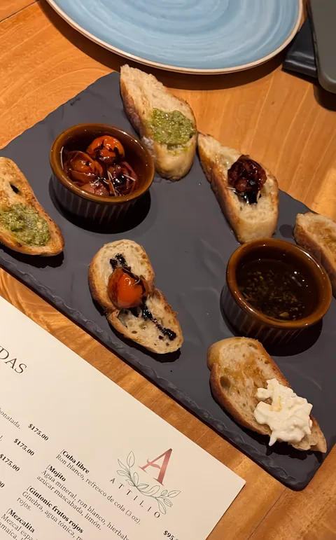 Tabla de pizarra con pan tostado: pesto, jitomate cherry con balsámico, burrata y dos cazuelitas de aceite