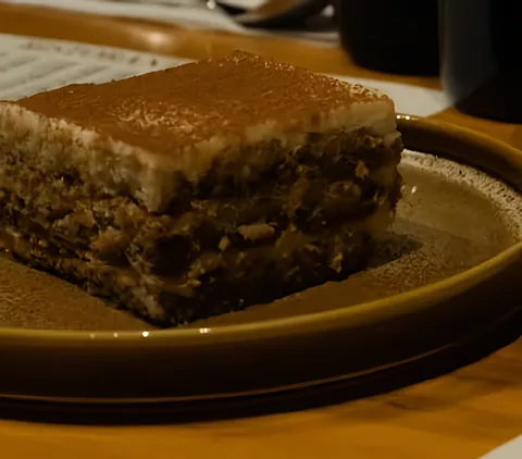 Rebanada de tiramisú espolvoreada con cacao en un plato de cerámica